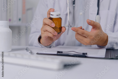 Cuadro en lienzo Doctor in white lab coat holds a brown medicine bottle and gestures with hand