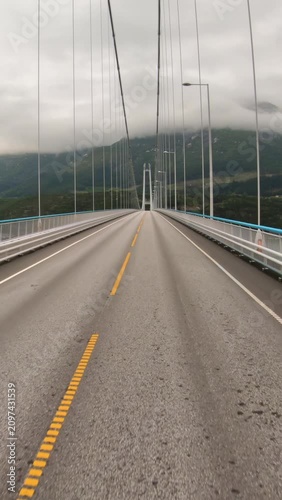 Car driving on a long bridge in Norway with misty mountains ahead.