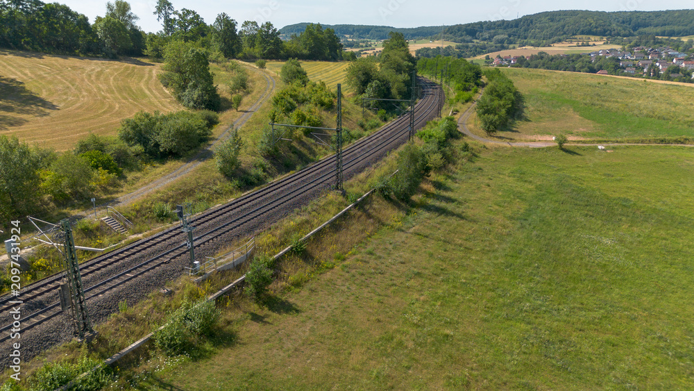 Fototapeta premium Aerial view of railway line winding through rural countryside with fields, forest and distant village