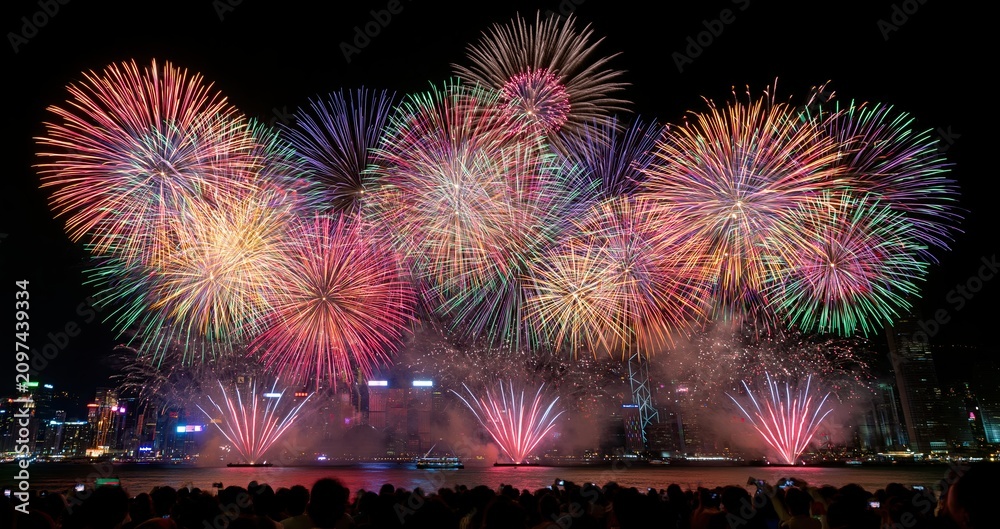 Fototapeta premium At midnight, colorful fireworks light up the night sky above a bustling city skyline during New Year’s celebrations.