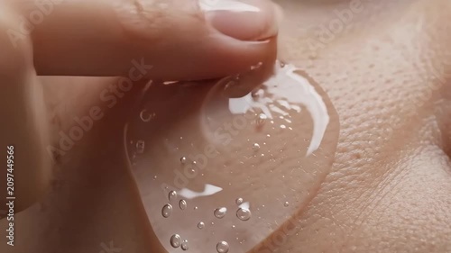 Extreme close-up of clear hyaluronic acid serum applied to skin. Finger spreading hydrating gel from a glass dropper. Skincare and beauty routine concept