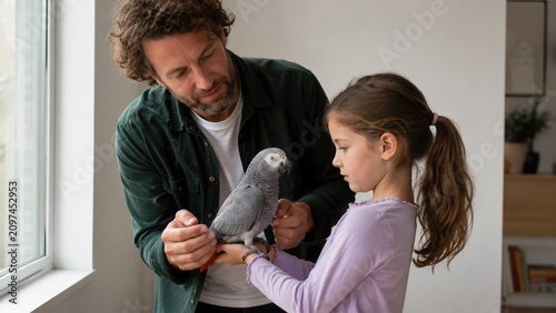 Father and daughter interact with African grey parrot indoors. Calm family moment exploring nature. Ideal for pet care, parenting, or education content.