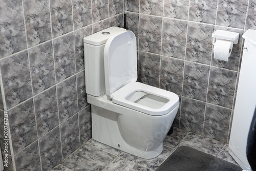 Close-up of a modern white ceramic toilet with an open lid against grey marble-patterned tiles.