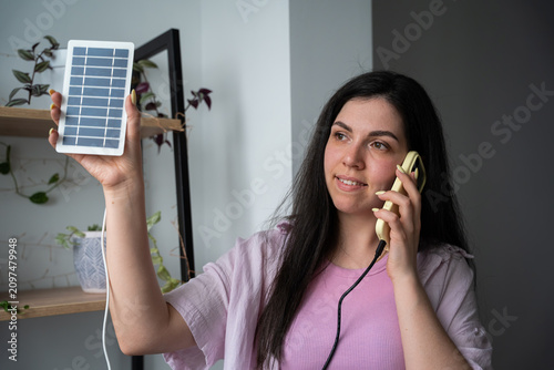 Young woman discussing solar panel options over phone indoors. Renewable energy consultation and green technology customer support