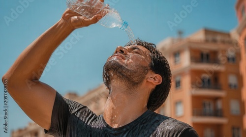 Man pouring water on face to cool down during a hot summer heat wave in a sunny city street.