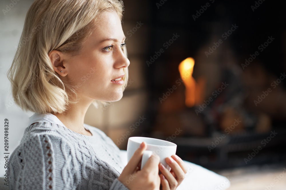 Obraz premium Fireplace, home and woman with coffee, thinking and contemplating decision with hot drink in lounge. Remember, memory and person with warm beverage on weekend, space and reflection with tea in house