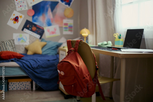 Foto Wide shot of child bedroom showing backpack hanging on chair beside laptop desk, suggesting home study routine and school readiness