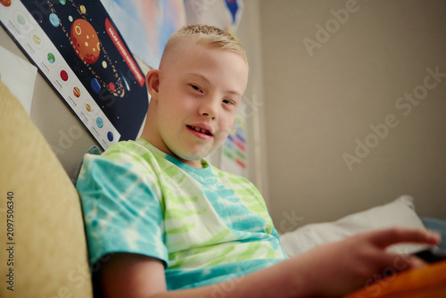 Obraz na płótnie Portrait of Caucasian child with Down Syndrome using tablet while sitting indoors, supporting inclusive learning and digital access