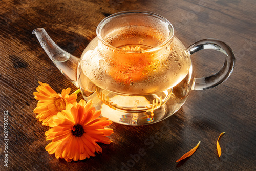 Calendula Tea. Vibrant orange marigold flowers infusing in a clear glass teapot