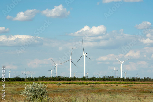 Wind turbine in a field generating clean renewable green energy under a blue sky with clouds.