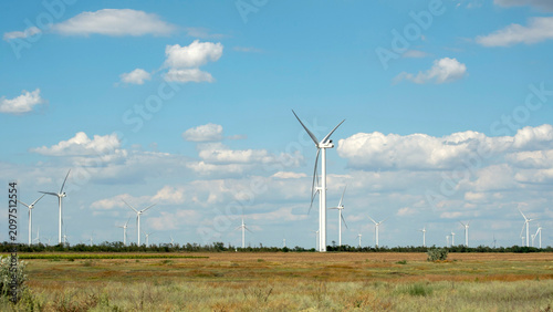 Wind turbine in a field generating clean renewable green energy under a blue sky with clouds.