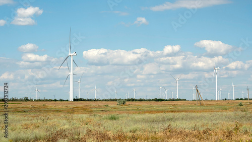 Wind turbine in a field generating clean renewable green energy under a blue sky with clouds.
