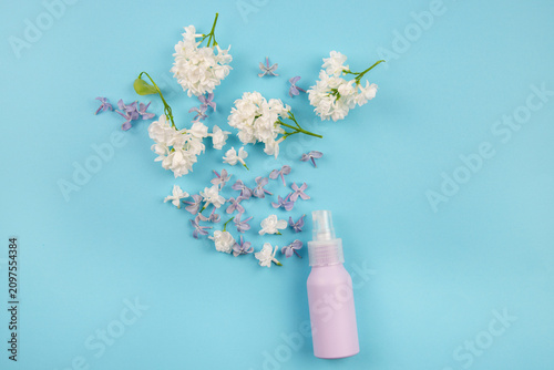 Homemade hydrosol or hydrolat, also known as flower water or lilac hydrosol. Purple spray bottle on a blue background, decorated with lilac Syringa vulgaris flower petals.