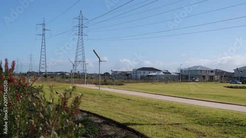 Large steel high-voltage electricity transmission towers and power lines run parallel to a public reserve and pedestria path in suburb of Tarneit, Melbourne Australia. Family homes borders easement