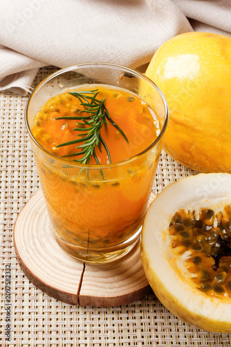 Glass of fresh passion fruit juice with natural pulp and rosemary garnish served beside ripe passion fruit.