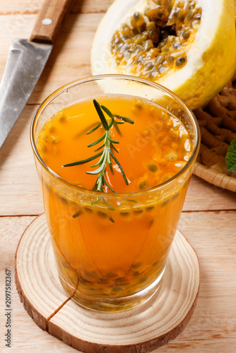 Fresh passion fruit juice with natural pulp served in a glass with rosemary garnish beside sliced tropical fruit.