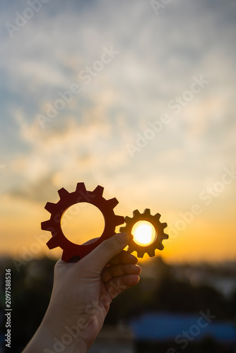 Hand holding wooden gears against the sunset sky. Concept of business strategy, cooperation, teamwork, efficient process, and engineering solutions for successful project management and development.