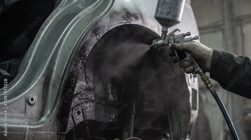 Naklejka premium Mechanic applies undercoating spray to a car's wheel arch for rust prevention and sound dampening. Automotive bodywork and protection process.