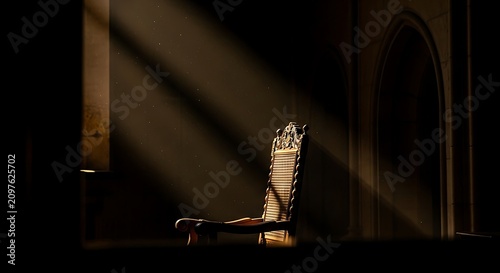 A dimly lit room with a single chair illuminated by sunbeams