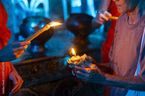 Foto Elderly person holding lotus candle while devotees light offering candles in tem
