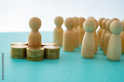 Concept of wealth concentration, economic inequality, and privilege represented with wooden pawns and stacks of coins.