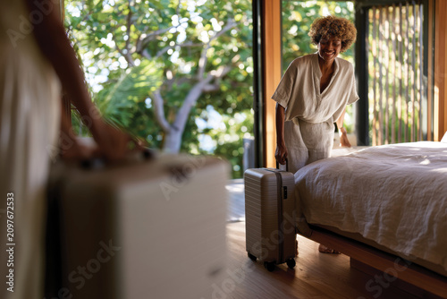 A warm and welcoming scene of a woman arriving at her eco-friendly retreat, showcasing happiness and relaxation while surrounded by vibrant greenery and natural beauty.