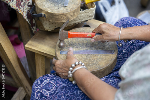 Obraz na plátně Handcrafted jewelry artisan hammering metal strip on wooden stump, focused hands