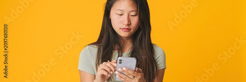 Quadro su tela Thoughtful girl in gray top scrolling on smartphone screen, looking at mobile ph