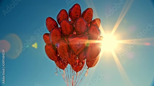 Giant red balloons float in the sky near the sun on a clear day in the city park