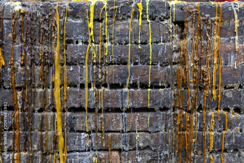 Obraz premium Melted colored wax dripping down rough brick wall, yellow and brown streams creating textured vertical patterns and weathered, layered surface with glossy drips and residue