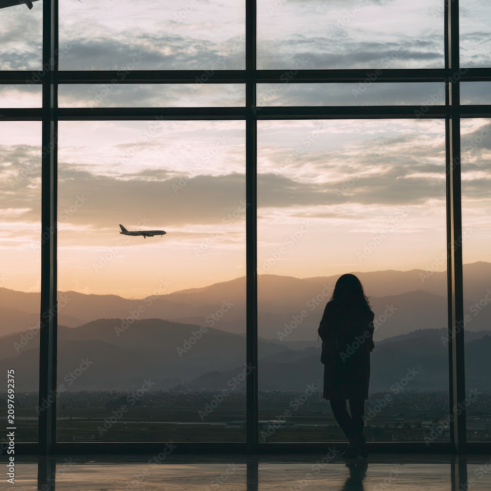 Fototapeta premium Travelers watch planes in the sky during sunset at an airport terminal with mountains in the background