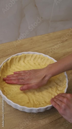 Woman's hands flattening shortbread dough into a white ceramic baking dish on a wooden table