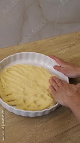 Woman's hands flattening shortbread dough into a white ceramic baking dish on a wooden table