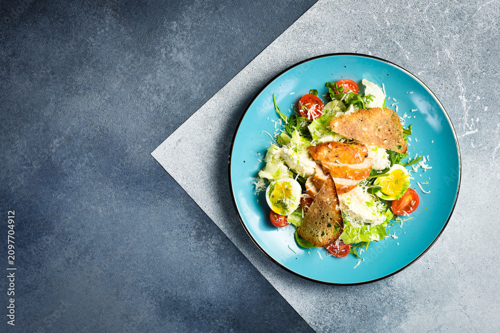 Obraz premium Fresh vegetable salad with chicken fillet and egg. Traditional Caesar salad. In a blue plate.