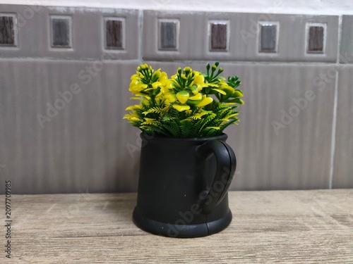 Artificial Yellow Flowers in Modern Black Mug on Wooden Surface. Minimalist Interior Decor for Home Office and Domestic Workspace. Flexible Layout.