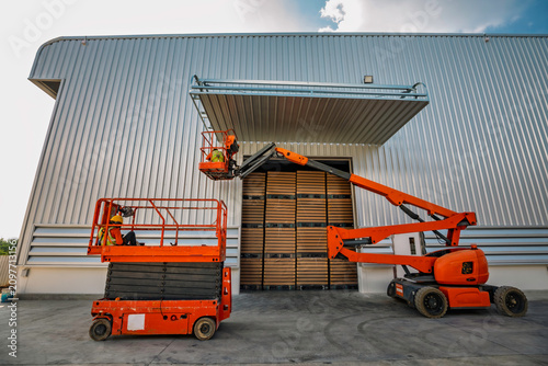 Workers are working on the Orange articulate boom lift or telescopic boom lifts and bucket crane mounted on truck for working at heights and articulating boom