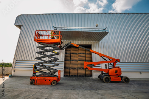 Workers are working on the Orange articulate boom lift or telescopic boom lifts and bucket crane mounted on truck for working at heights and articulating boom