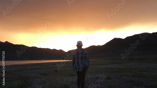 A woman with a dog on a mountain ridge looks at a vibrant sunset sky. Outdoor lifestyle photo with copy space for travel, adventure, and recreation commercial concepts.
