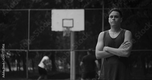 Fotografi Young man standing on basketball court with arms crossed, confident and focused