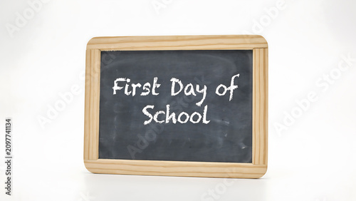 First day of school message written in white chalk on a small wooden framed blackboard isolated on a plain white background, educational concept