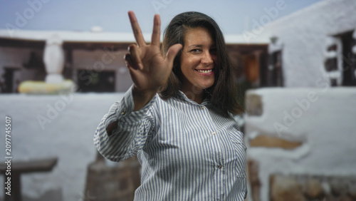 Photography Woman face smiling with arms raised, hair flipping, wearing striped shirt while standing before a textured wall mural in studio; joy celebration
