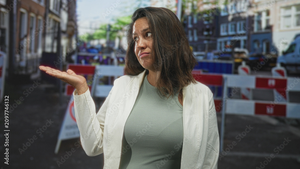 Fototapeta premium Woman shrugging with palm up hand at a blocked urban street with construction barriers and vans, looking unimpressed; frustration inconvenience.