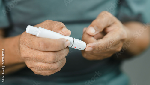 Fotografie Close-up of a senior adult using a lancet device for finger prick blood glucose testing at home