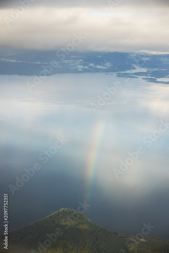 Rainbow arc bending over forest hill and lake