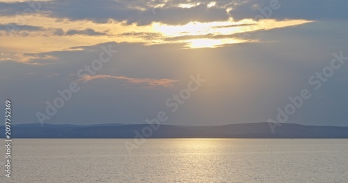 Sun setting over calm lake water and distant mountains