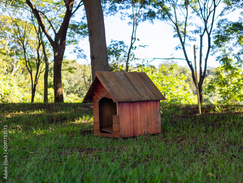 Casinha para cachorro feita de madeira na grama em um parque arborizado / Wooden dog house on the grass in a wooded park