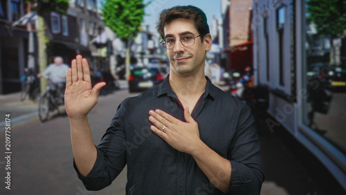 Foto Man raising palm and placing other hand on chest in a pledge gesture on a busy street lined with shops and bicycles; sincerity honor