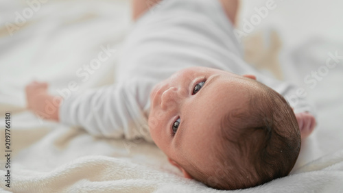 Konstfotografi Newborn boy lying on soft blanket, head turned with eyes gazing and tiny fist raised in studio; tenderness serenity