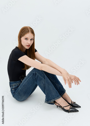 Cute girl posing sitting in jeans on a light background