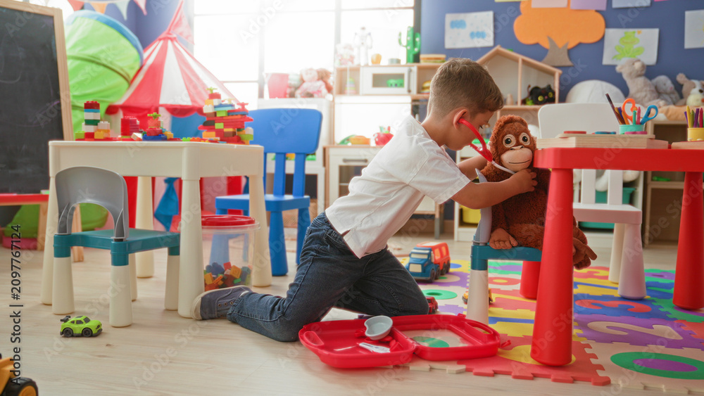 Obraz premium Boy kneeling, holding a toy stethoscope and medical kit with hands on alphabet foam mat in preschool; playful imagination.